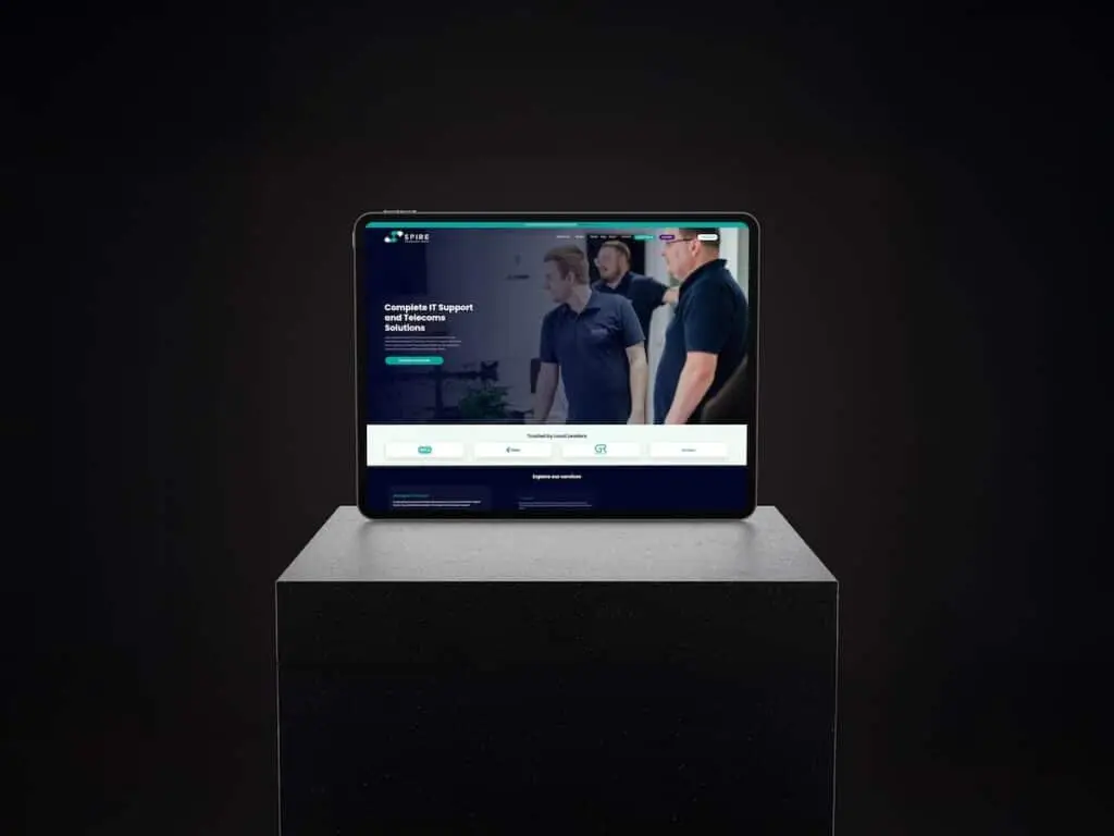 Tablet on a black pedestal displaying a blue IT services website on a dark background.
