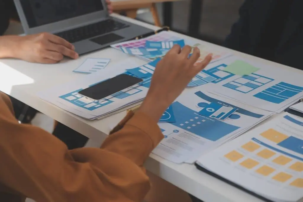 Person working at a white table reviewing blue and orange infographic sheets with a laptop nearby