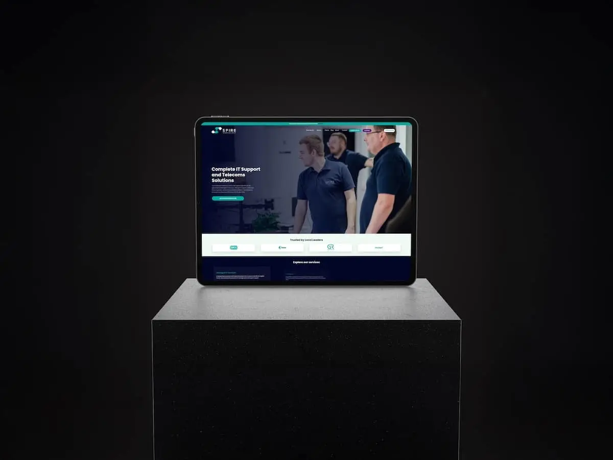 Tablet on a black pedestal displaying a blue IT services website on a dark background.